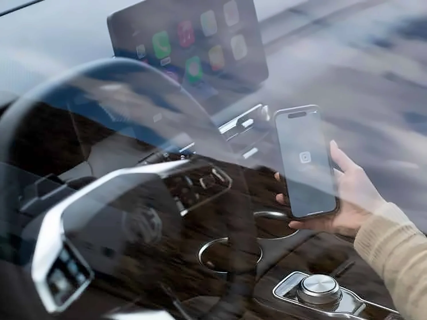 Driver holding a phone beside the infotainment screen Driver holding a phone beside the infotainment screen